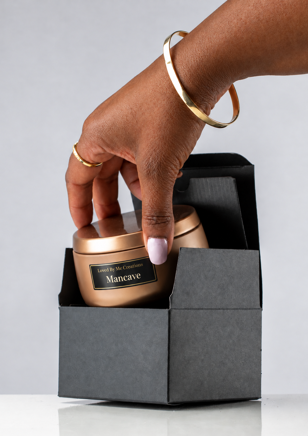 Mancave fragrance candle tin with small Loved By Me Creations label, held by a brown-skinned hand